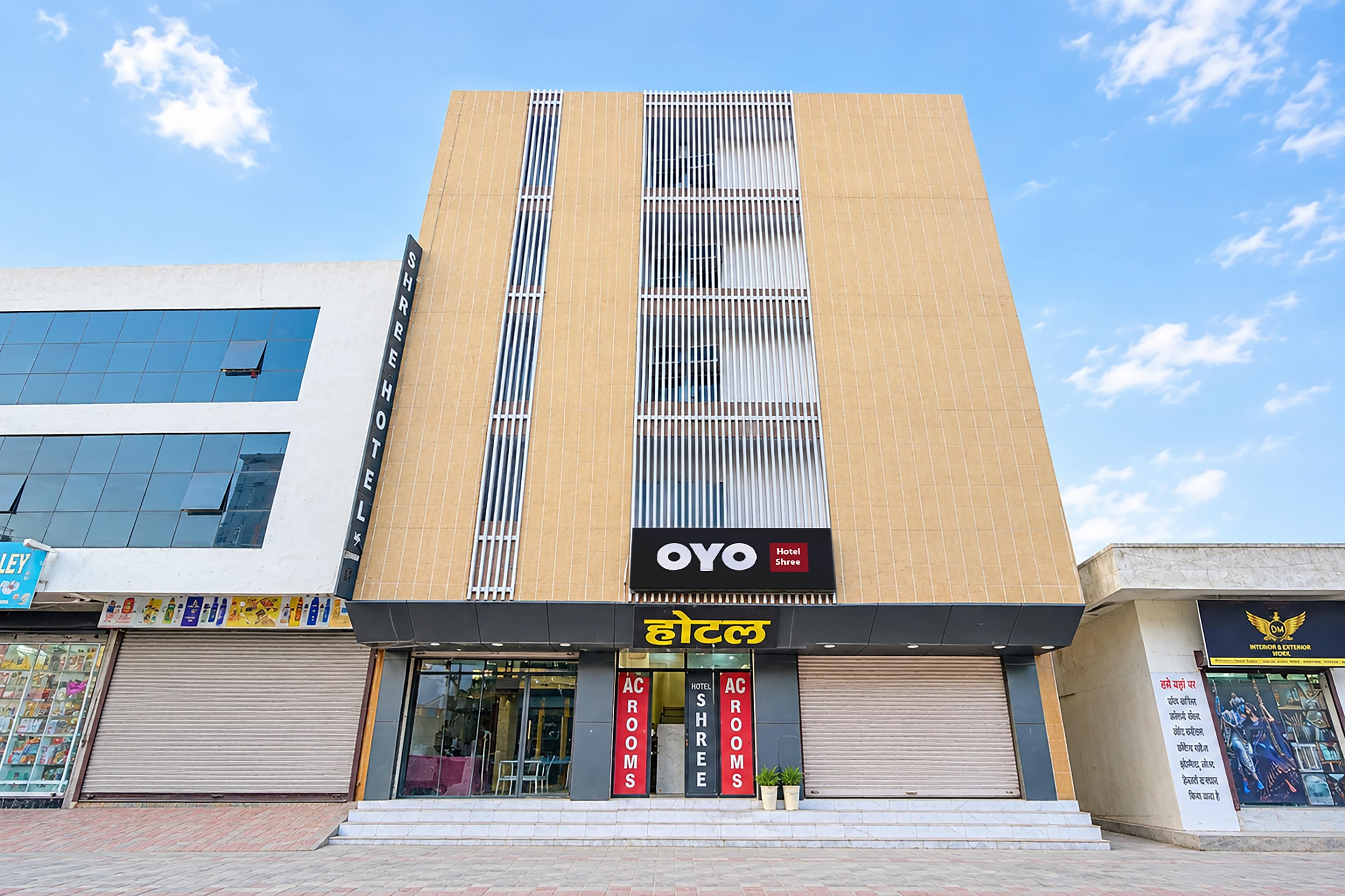 A hotel with a modern facade, featuring a prominent sign for 'OYO Hotel Shree' and 'AC ROOMS' indicating available accommodations.