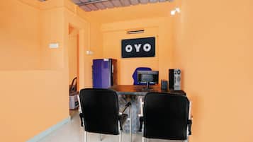 A small, orange-walled room with a desk, two chairs, a refrigerator, a computer, and a sign that reads 'OYO'.