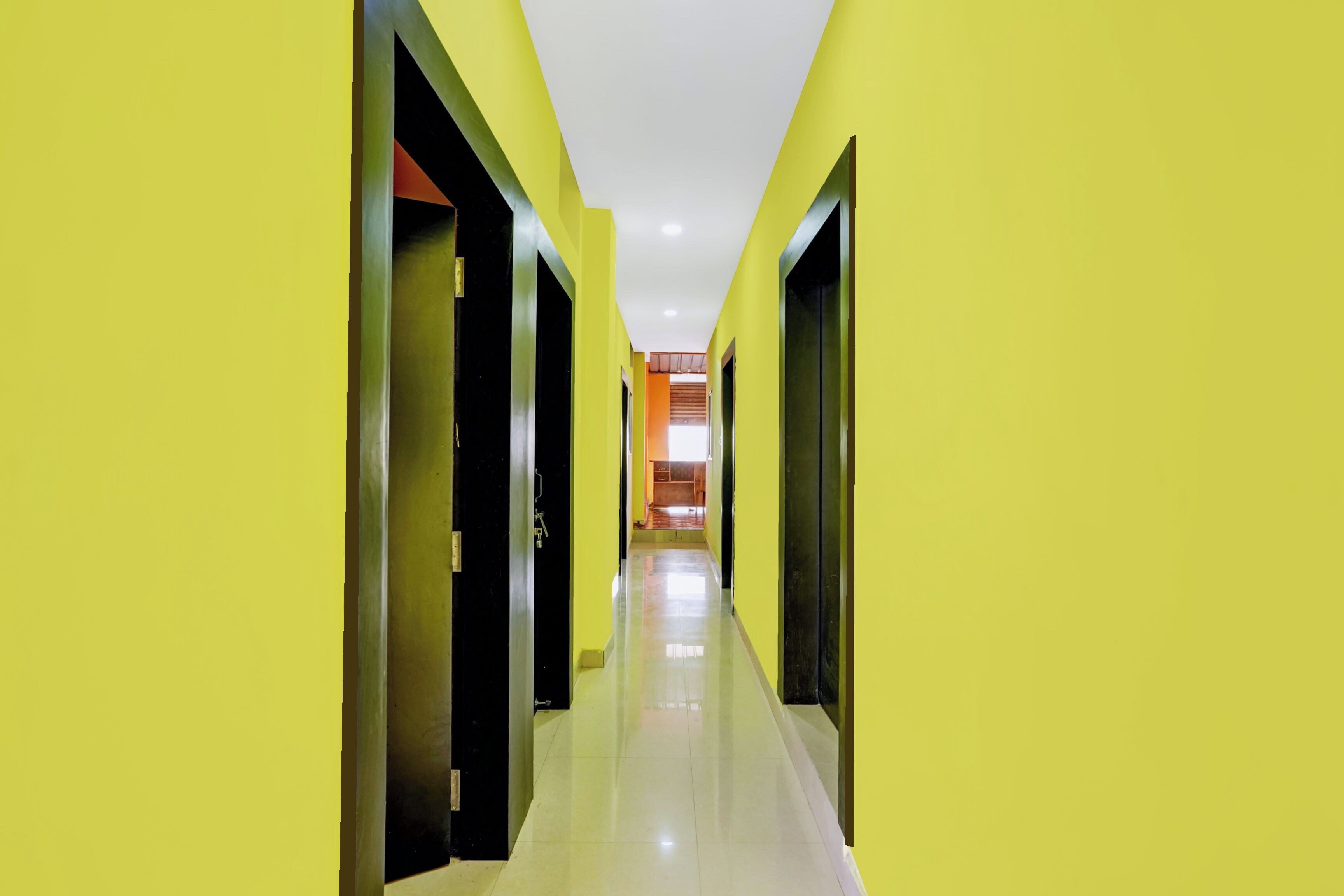 A corridor with yellow walls and doors, leading to a room with a wooden floor and a view of a kitchen area.