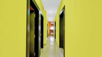A corridor with yellow walls and doors, leading to a room with a wooden floor and a view of a kitchen area.