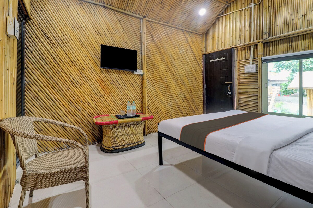 Une chambre avec un lit, un téléviseur fixé au mur, une petite table avec des bouteilles et un fauteuil en osier.
