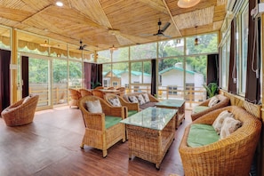 A spacious room with wicker furniture, large windows, and a ceiling fan. - Hotel O by OYO Tapovan Rise cottages and (Rishikesh)