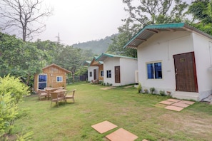 A row of small, single-story cottages with a grassy yard and a wooden deck. - Hotel O by OYO Tapovan Rise cottages and (Rishikesh)