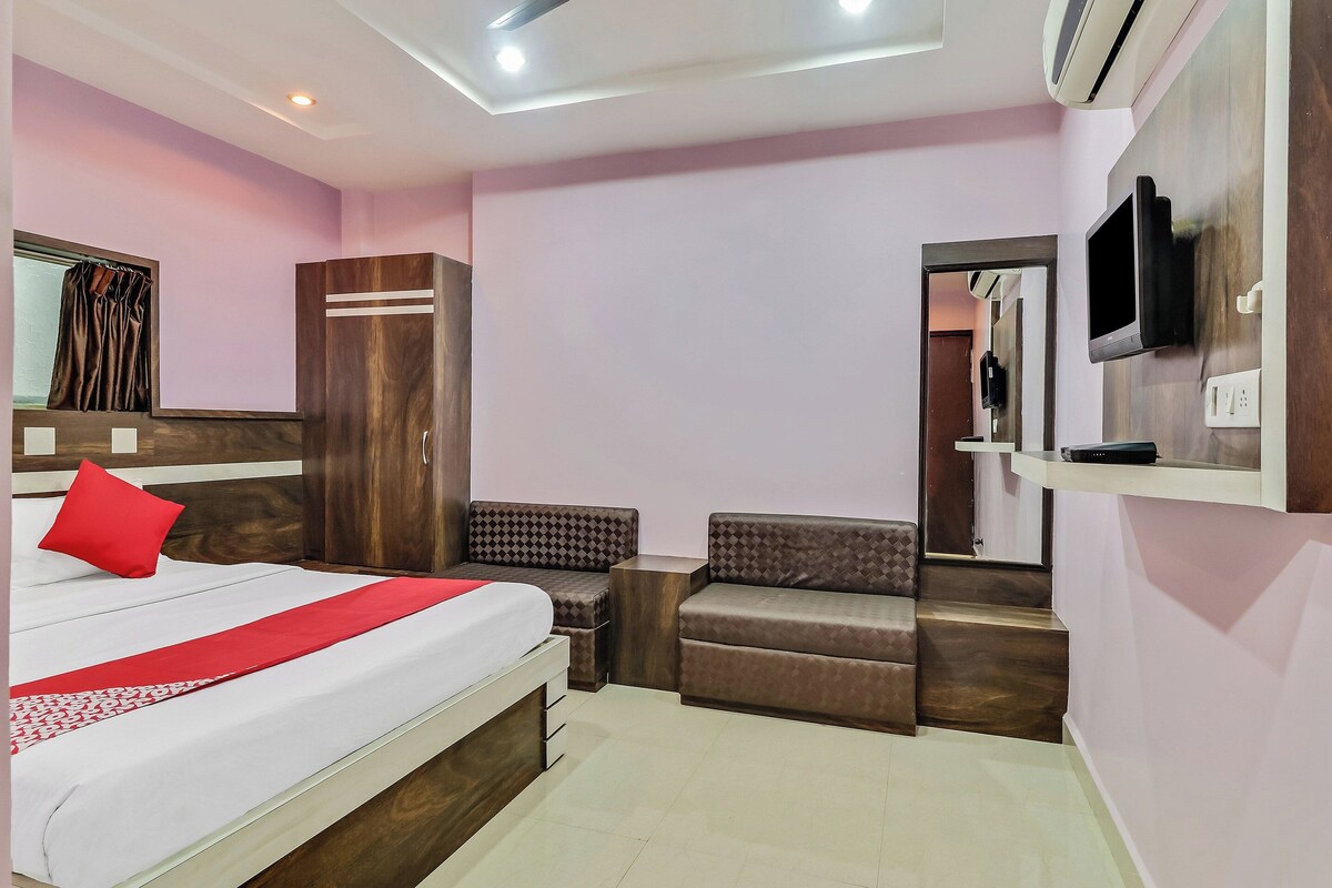 A hotel room with a bed, a wardrobe, a seating area, and a television.