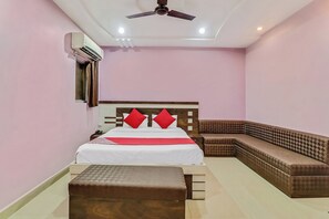 A hotel room with a bed, a sofa, a bench, a ceiling fan, and an air conditioning unit. - Hotel O Royal (Rajnandgaon)