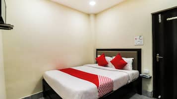 A hotel room with a bed, a red and white bedspread, a black headboard, a white wall, a door, and a light switch.