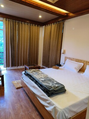 Un dormitorio con una cama grande, piso de madera, una mesita de noche y cortinas.