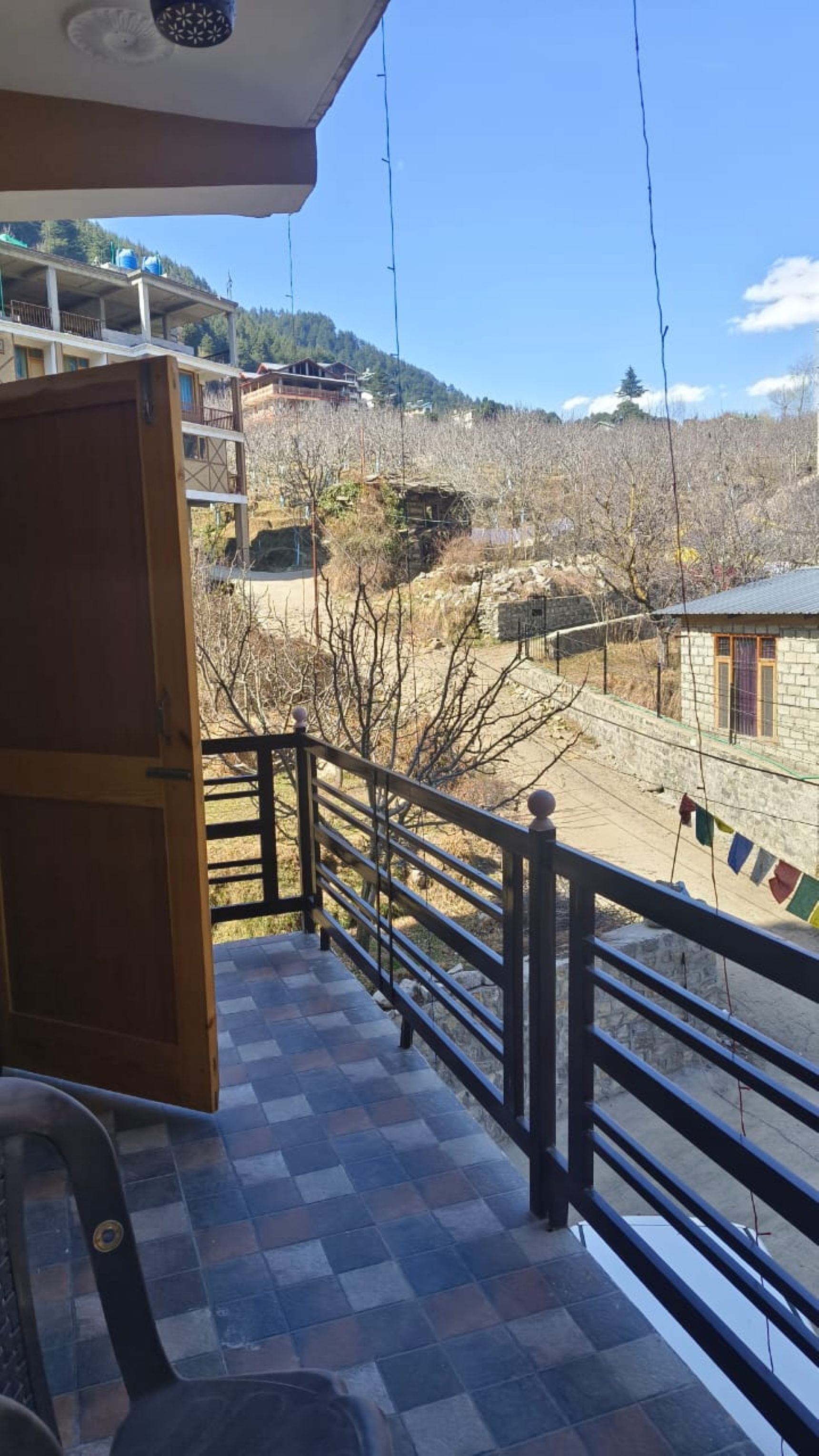 A balcony with a checkered floor, a railing, and a view of a mountainous landscape with buildings.