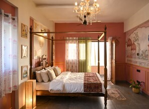 Een hemelbed met een baldakijn, een kroonluchter en een groot raam met gordijnen.