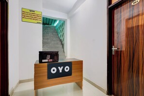 Balcão de recepção de hotel com uma placa indicando 'OYO' e uma escada que leva ao andar superior.