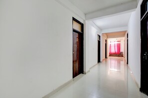 Un pasillo con paredes blancas y suelo de baldosas que conduce a una habitación con cortina roja.