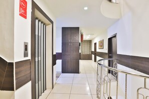 Un pasillo de hotel con barandilla de metal, una cámara de seguridad, una puerta con cortina estampada y un aplique en la pared.