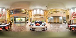 Um hall amplo com área de estar central, estantes de livros e um balcão de recepção.