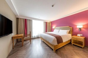 Quarto de hotel com cama, escrivaninha, cadeira, televisão e janela com cortinas.