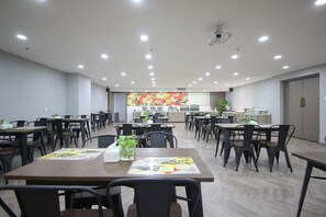 Uma sala de jantar espaçosa com várias mesas e cadeiras, uma área de cozinha ao fundo e um teto com iluminação embutida.