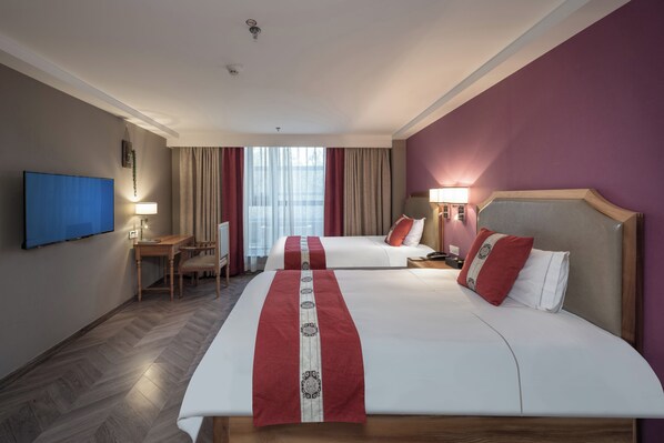 Quarto de hotel com duas camas, uma escrivaninha, uma cadeira, uma televisão e uma janela com cortinas.