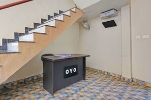 Una escalera con barandilla, un escritorio pequeño con un cartel y un ventilador en la pared.