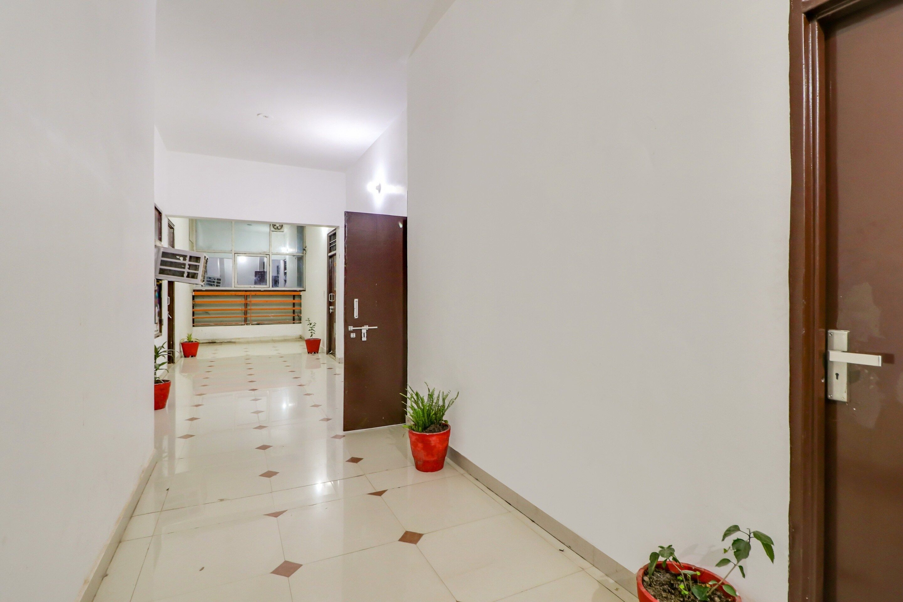 A hallway with a tiled floor, a door on the right, and potted plants along the walls.