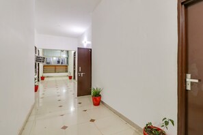 A hallway with a tiled floor, a door on the right, and potted plants along the walls. - Hotel O Olive (Rohtak)