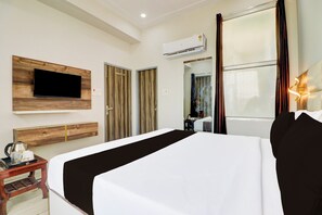 A hotel room with a bed, a flat-screen TV mounted on a wooden panel, a coffee maker on a side table, and an air conditioning unit on the wall. - Hotel O by OYO Gold Inn (Rohtak)