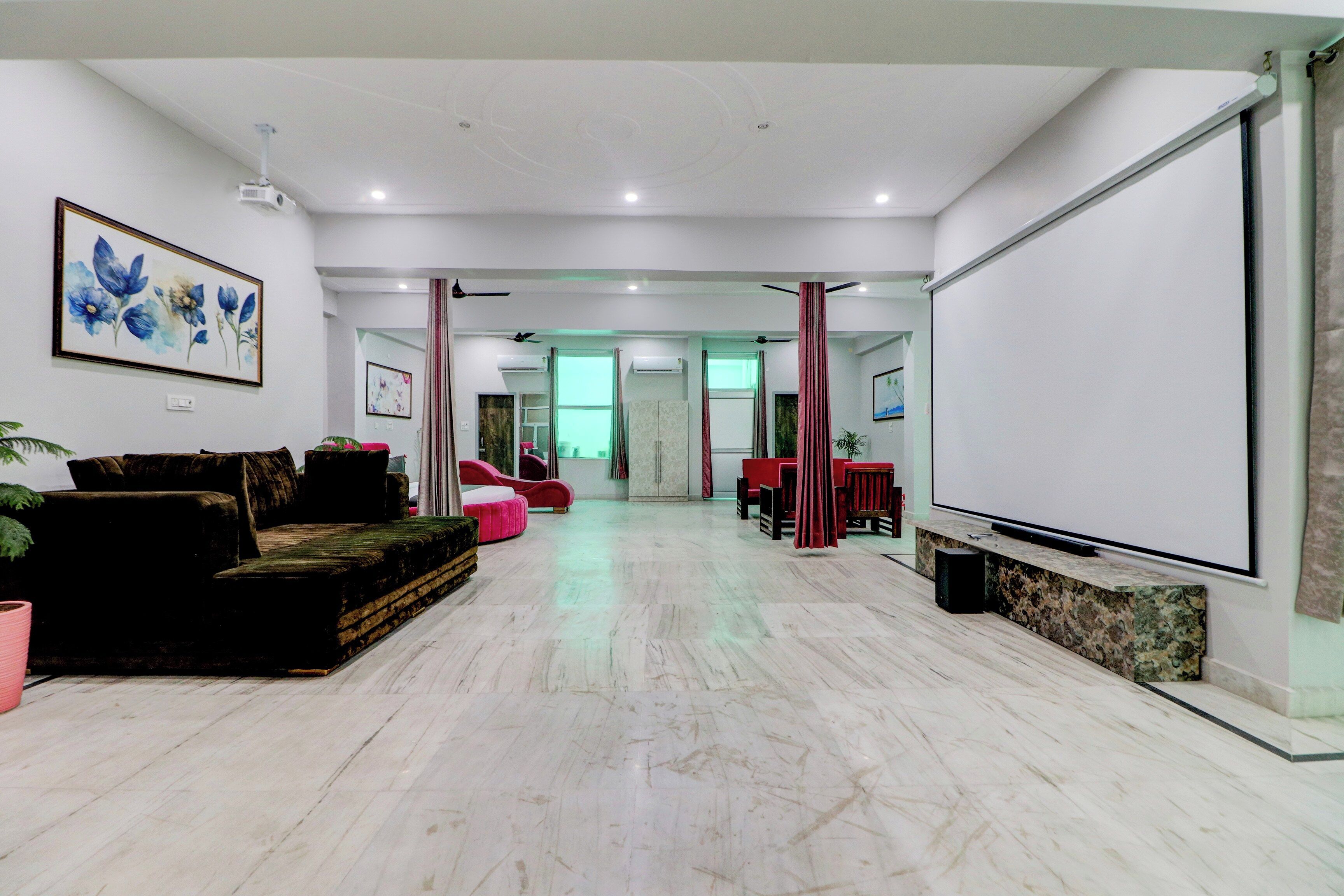 A spacious room with a large flat-screen TV, a sofa, a coffee table, and a potted plant.