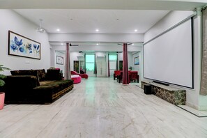 A spacious room with a large flat-screen TV, a sofa, a coffee table, and a potted plant. - Hotel O by OYO Gold Inn (Rohtak)