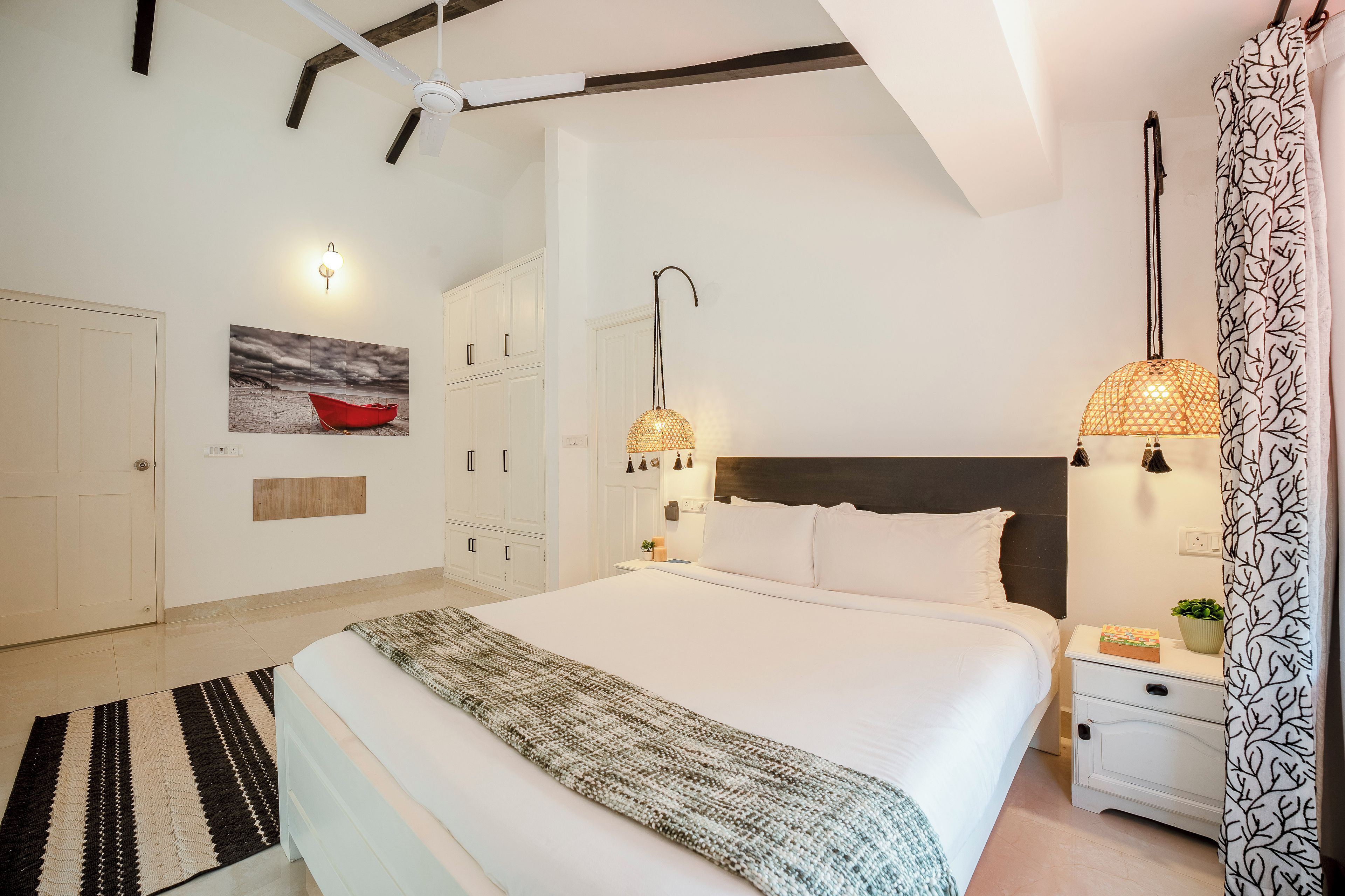 A bedroom with a large bed, a nightstand, a wall-mounted lamp, and a ceiling fan.