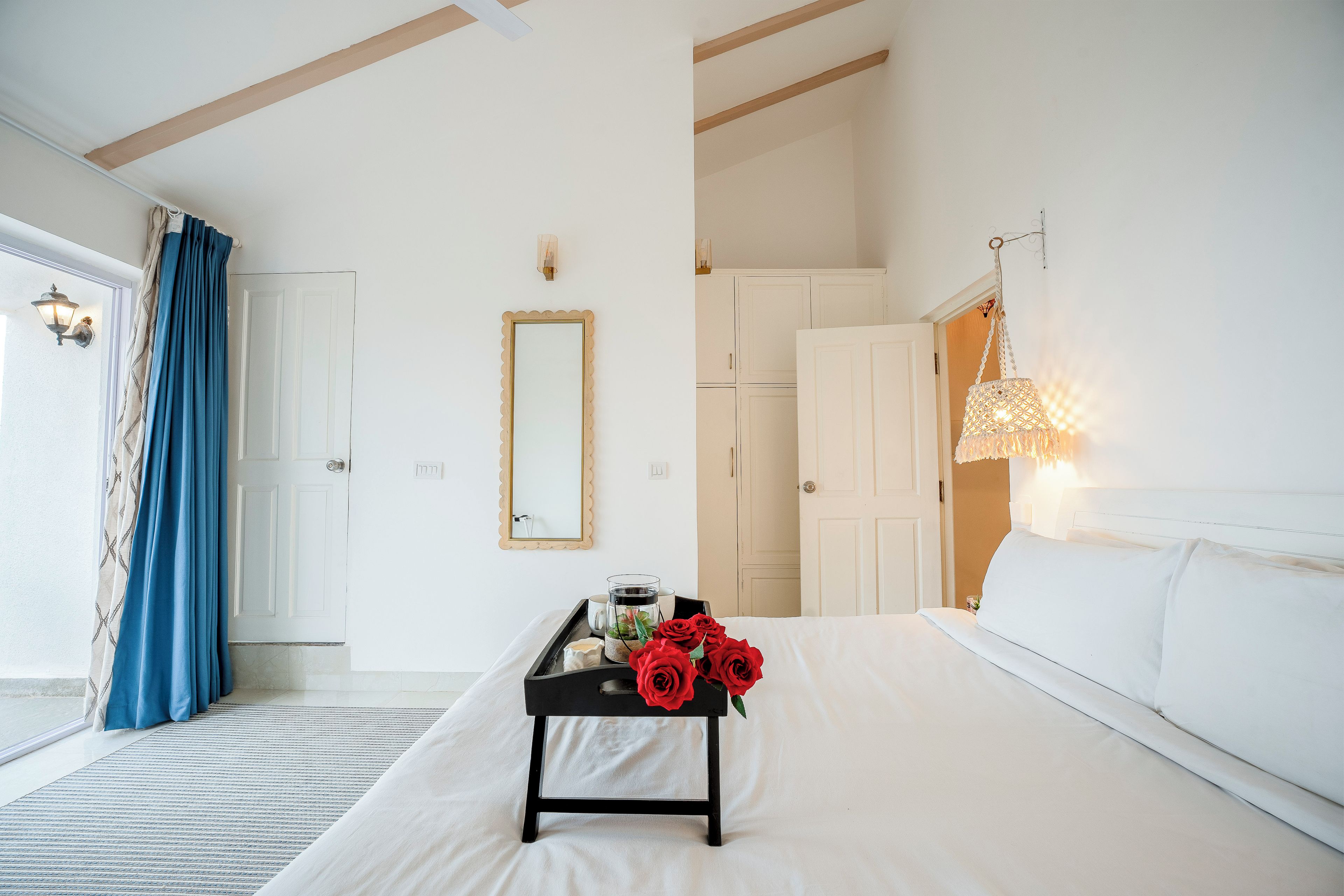 A hotel room with a bed, a bedside table with a tray of red roses, a mirror, and a hanging light fixture.