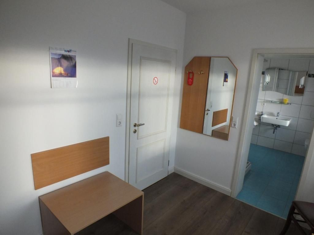 Habitación de hotel con un banco de madera, una puerta con letrero de prohibido fumar, un espejo y un baño con piso azul.