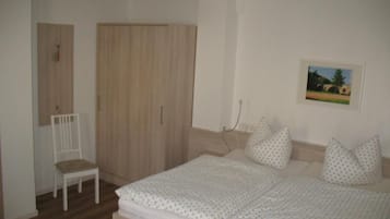 A bedroom with a bed, a chair, a wardrobe, and a picture on the wall.