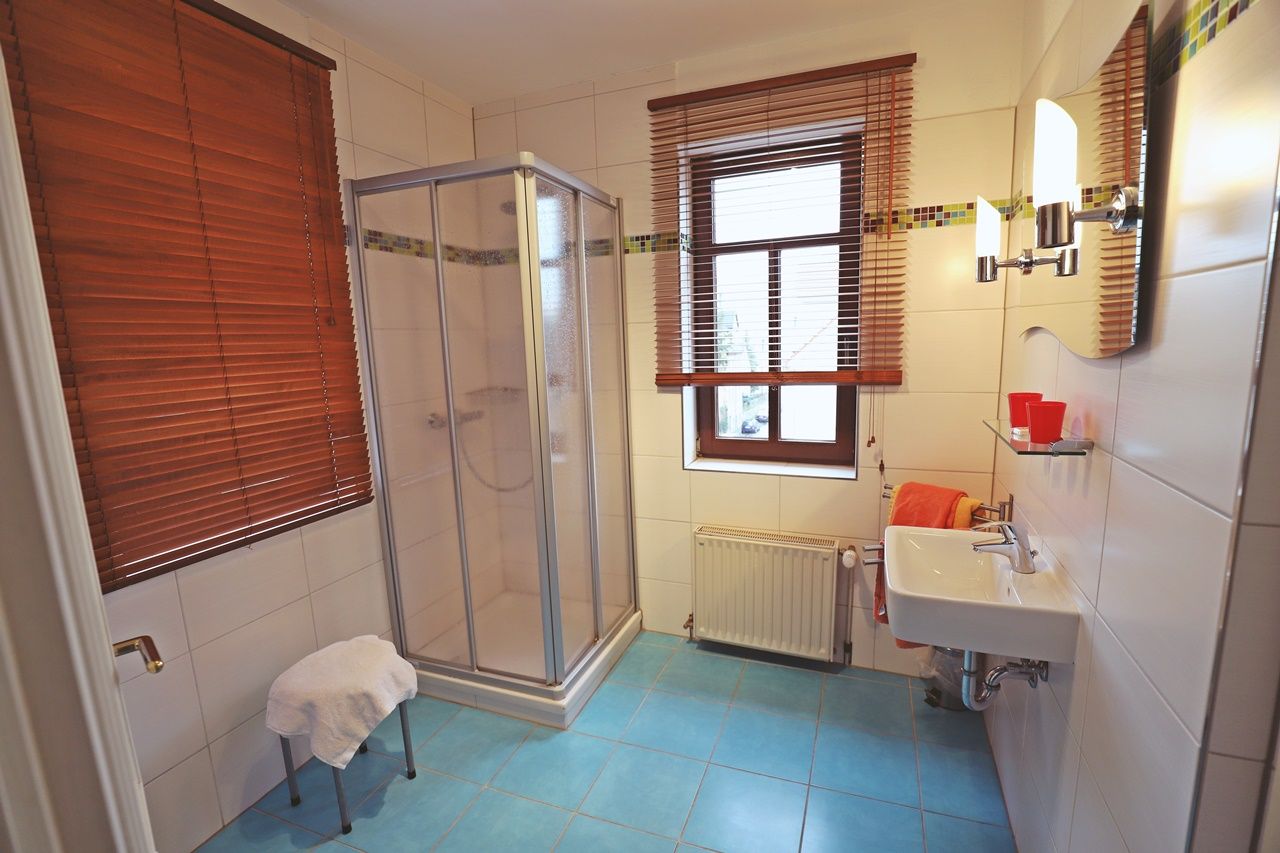 Ein Badezimmer mit Dusche, Waschbecken und einem Fenster mit Jalousien.