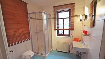 Ein Badezimmer mit Dusche, Waschbecken und einem Fenster mit Jalousien.