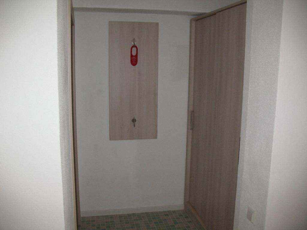 Une pièce avec une armoire en bois, une petite porte dotée d’une poignée rouge et un sol carrelé.