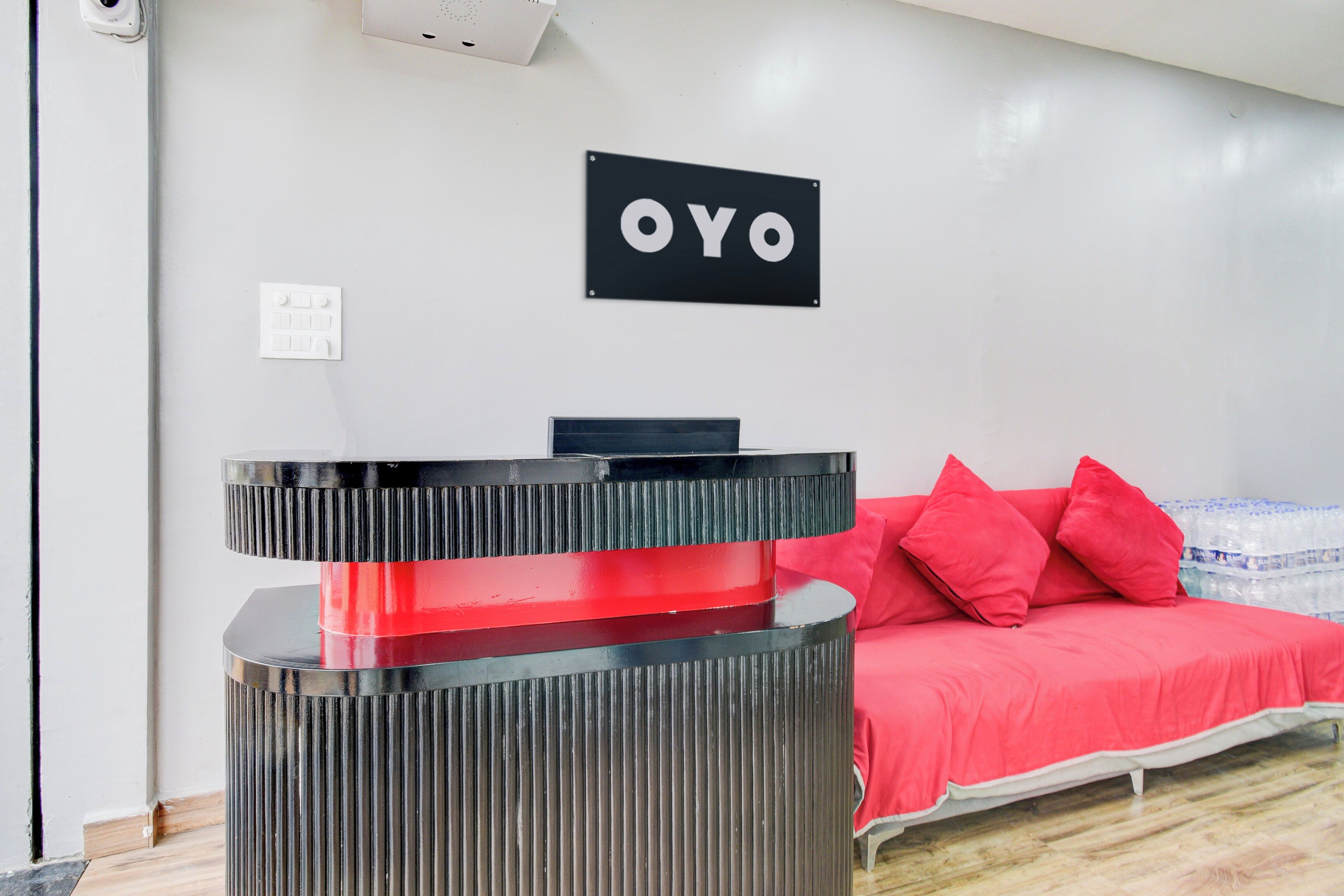 A hotel reception desk with a black and red design, a bed with red bedding, and a sign that reads 'OYO' on the wall.