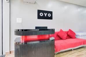 Un mostrador de recepción de hotel con diseño en negro y rojo, una cama con ropa de cama roja y un cartel en la pared que dice 'OYO'.
