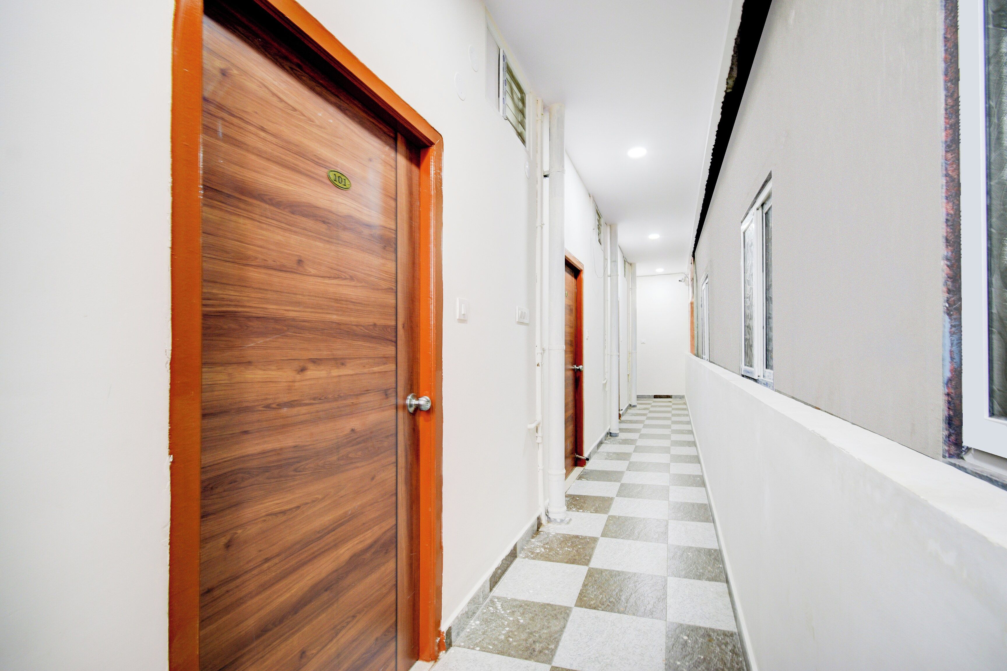 A corridor with wooden doors, white walls, and a checkered floor.