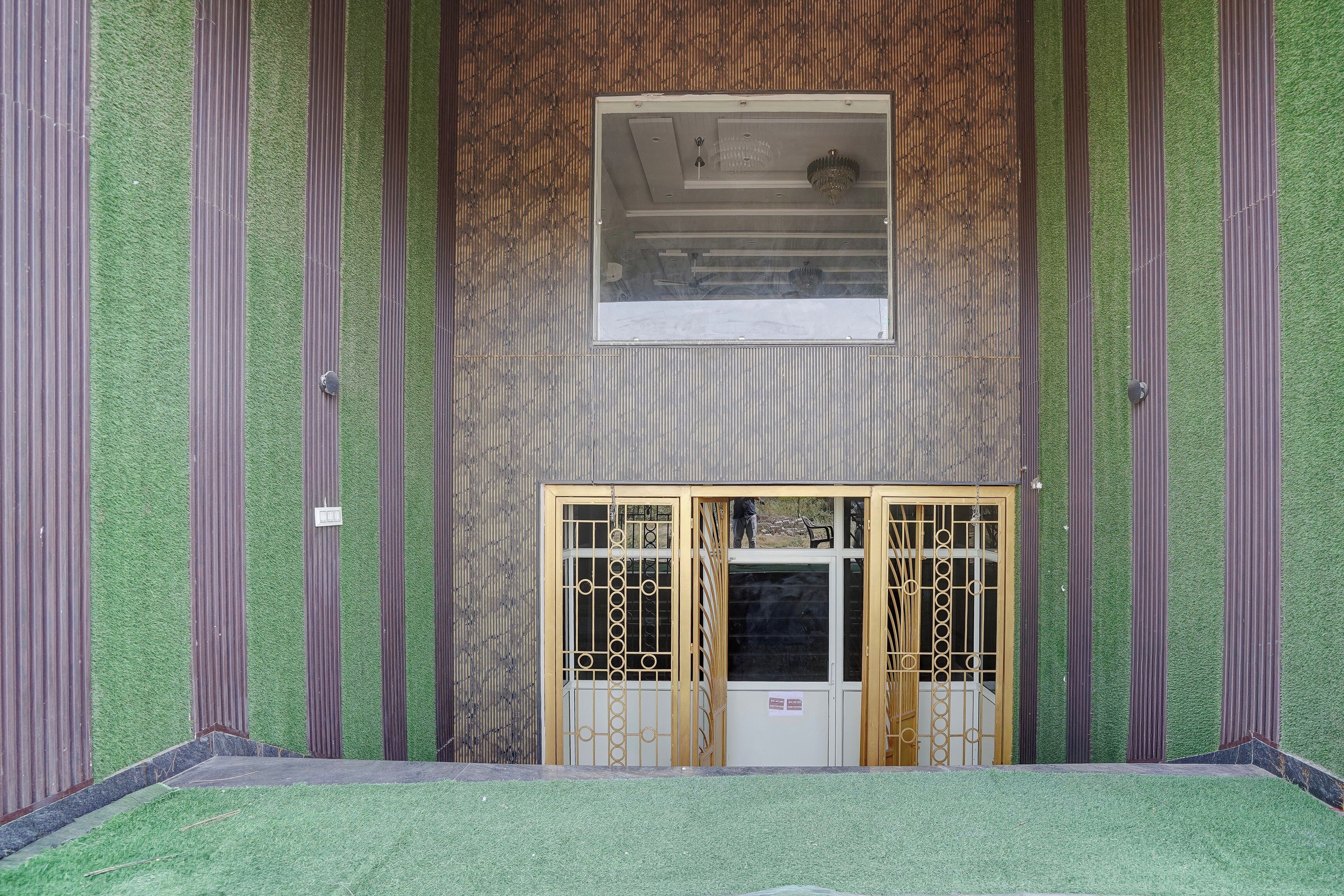 A room with a green artificial grass floor, a wooden door with a metal gate, and a wall with vertical wooden slats.