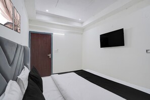 Habitació d'hotel amb un llit, una televisió penjada a la paret i una porta que dona a una altra habitació.