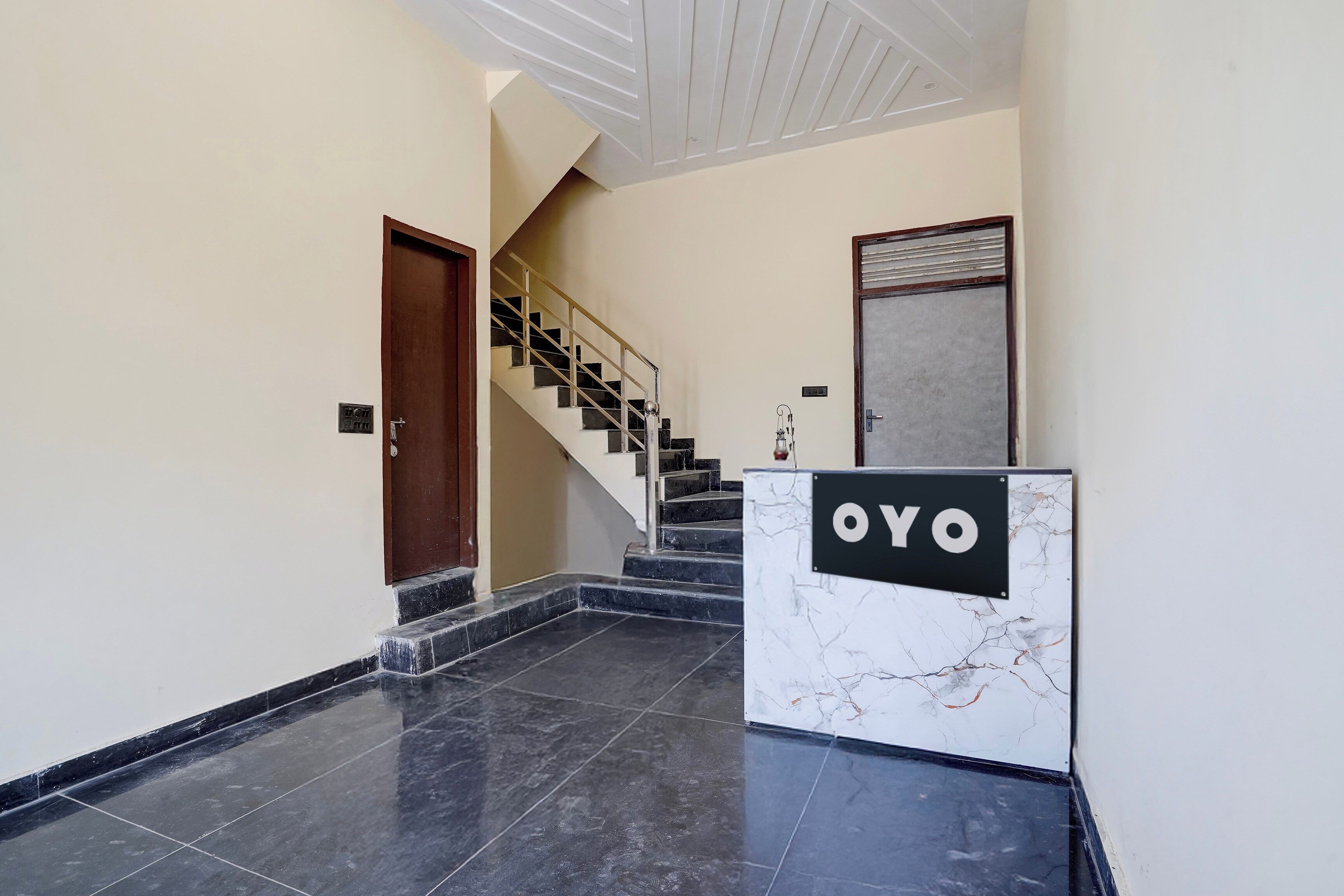 A hotel lobby with a marble reception desk, a staircase, and a wooden door.