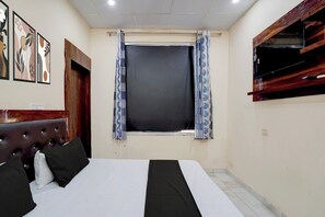 Habitació d'hotel amb un llit, una finestra amb cortines, una televisió penjada a la paret i una paret amb obra enmarcades.