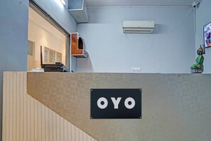 Zona d'estació amb un rètol que diu 'OYO' a una paret amb textura, una unitat de aire condicionat penjada a la pared, i una petita estàtua de Buda a la dreta.
