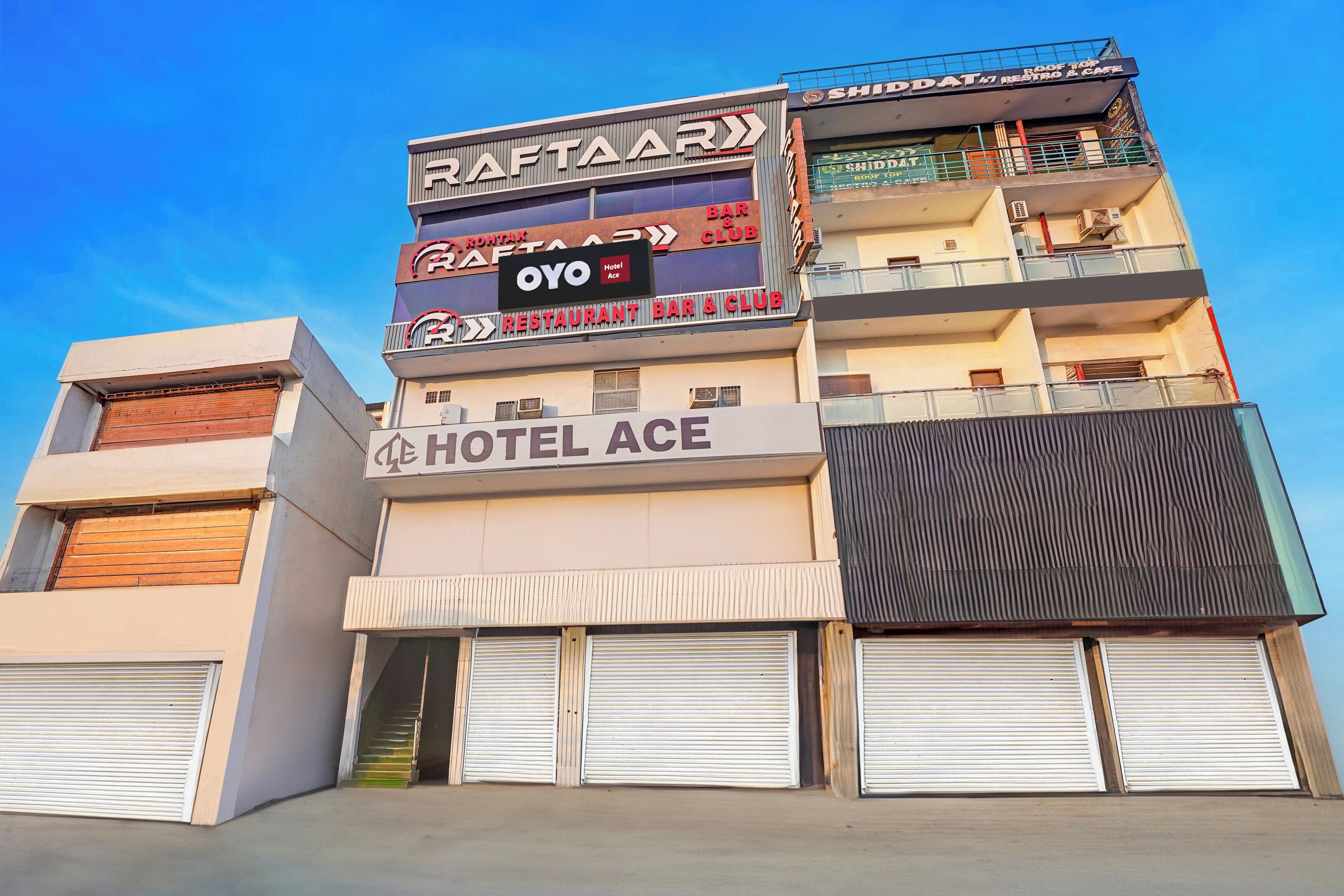 A multi-story building with a sign for 'ROOF TOP RESTAURANT & CAFE' and 'HOTEL ACE' on the ground floor.