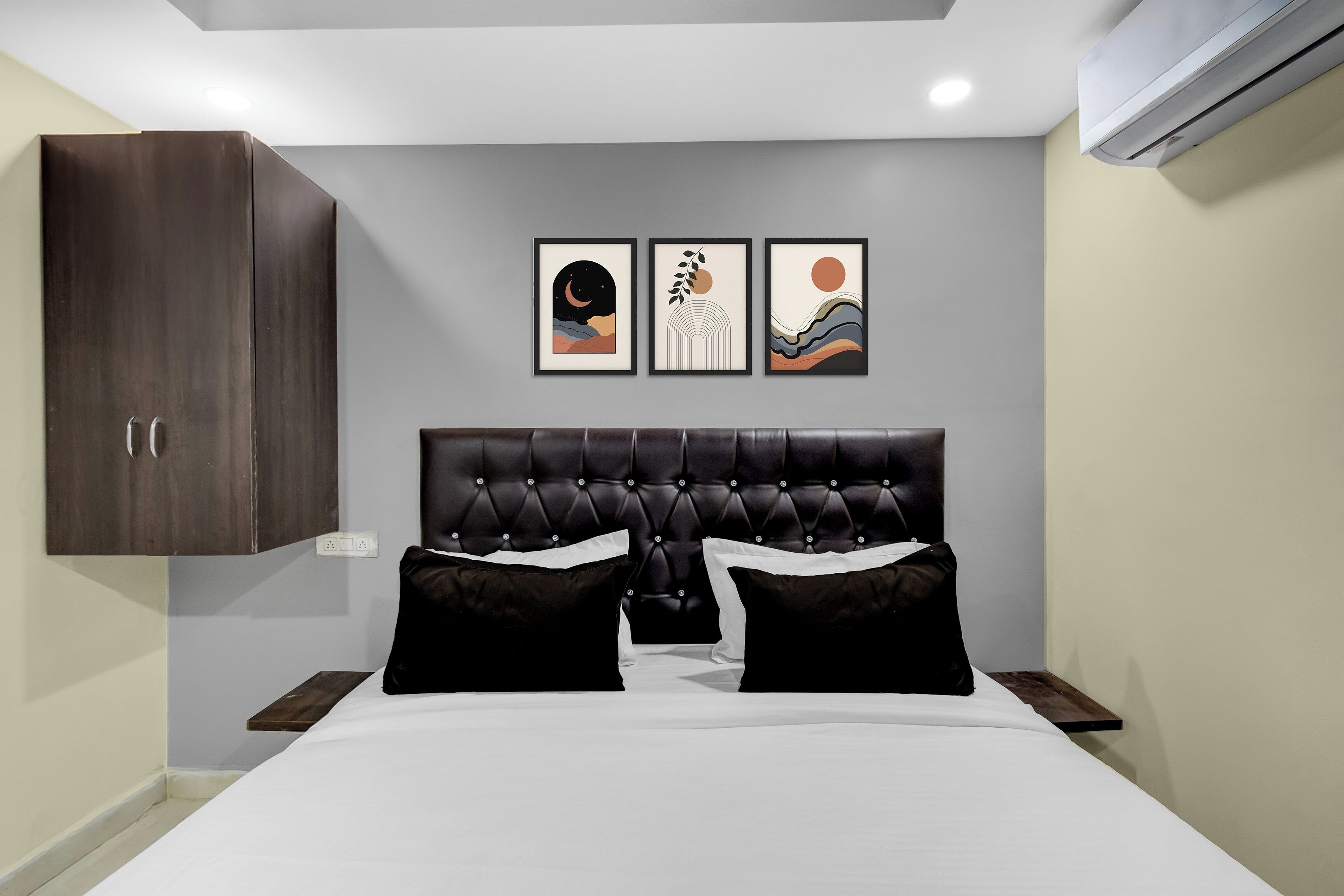 A bedroom with a tufted headboard, a bed with white linens, two black pillows, and three framed artworks on the wall.