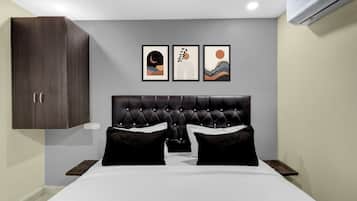 A bedroom with a tufted headboard, a bed with white linens, two black pillows, and three framed artworks on the wall.