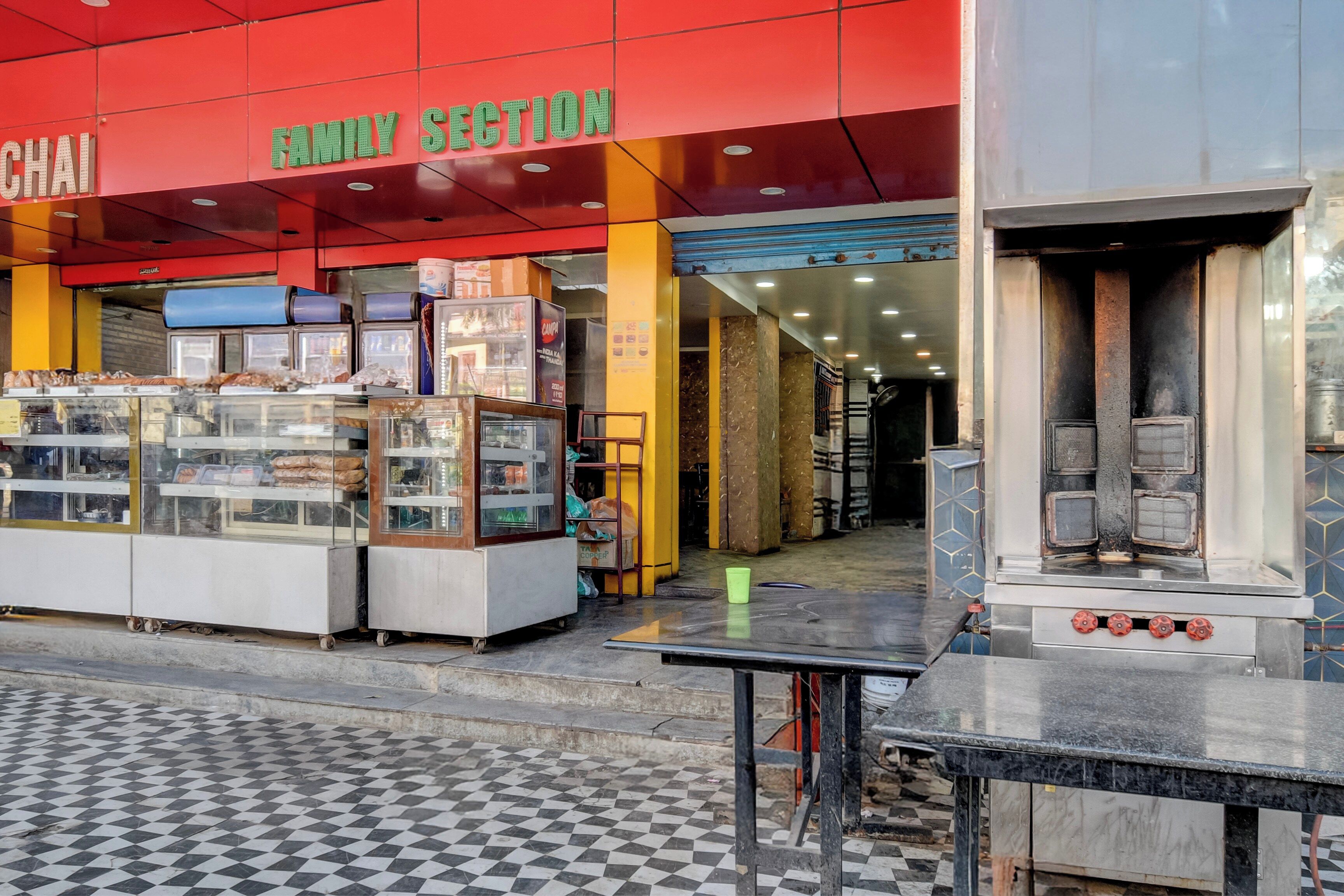 Un puesto de comida con una vitrina de vidrio y un mostrador, ubicado frente a un edificio con toldo rojo y un letrero que dice 'SECCIÓN FAMILIAR'.
