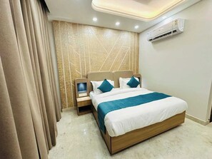 A hotel room with a large bed, bedside tables, an air conditioning unit, and a television on a stand. - Hotel O Bulbul Hotel (Rohtak)