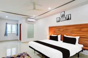 Ein modernes Hotelzimmer mit einem großen Bett, einem Deckenventilator, einer Klimaanlage und gerahmten Bildern an der Wand.