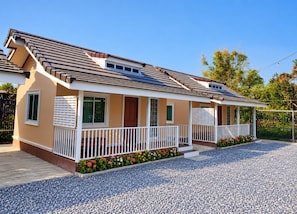A two-story house with a sloped roof, a front porch with white railings, and a gravel driveway. - Pakdee House Homestay (Ayutthaya)