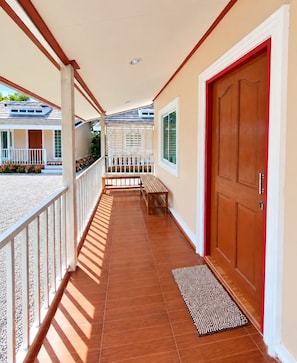 A covered corridor with a wooden bench, a red door, and a white railing. - Pakdee House Homestay (Ayutthaya)