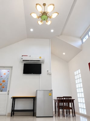 A room with a ceiling fan, an air conditioning unit, a flat-screen TV, a refrigerator, a wooden table, and a window. - Pakdee House Homestay (Ayutthaya)